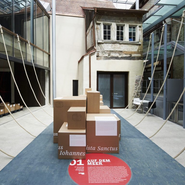 Foto des Innenhofs des Humpis-Quartiers, abstrahierte Darstellung eines Schiffsbauchs mit Hilfe von Tauen, Pappkisten mit lateinischen Namen